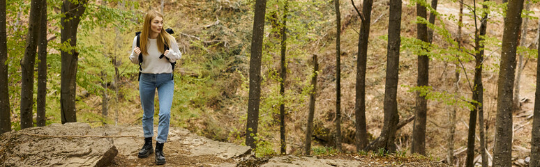 blonde woman hiker with backpack walking through the forest discovering new paths, banner