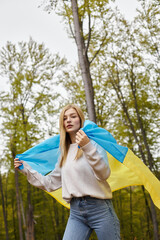 Patriotic blonde female adventurer proudly holding national Ukrainian flag in forest, freedom