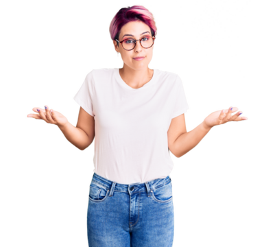 Young beautiful woman with pink hair wearing casual clothes and glasses clueless and confused expression with arms and hands raised. doubt concept.