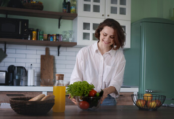 Young Woman sorting green fresh vegetables from shopping bag while standing in kitchen at home