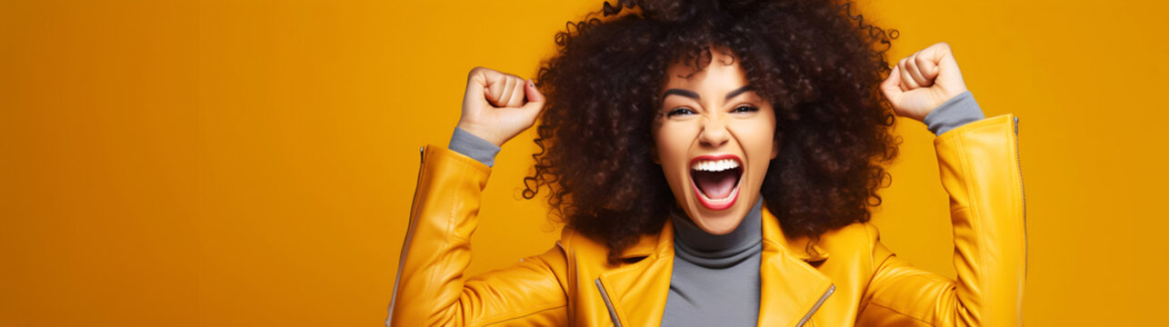 Woman shouts with enthusiasm and raises her fist in victory against vibrant yellow backdrop, celebrating her triumphant win in the lottery with ample negative space for text
