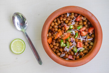 Boiled chickpeas in an earthen pot on wooden background. Chopped tomatoes, onion, and green chilies...