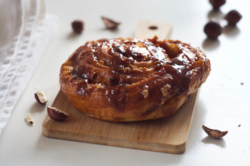 A bun with caramel and nuts lies on a board on the table.