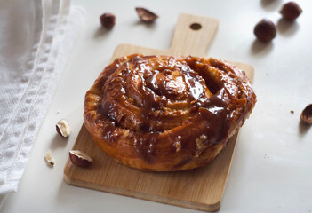 A bun with caramel and nuts lies on a board on the table.