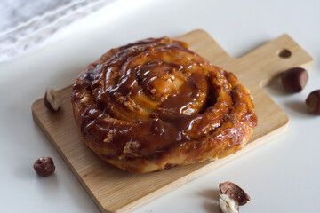 A bun with caramel and nuts lies on a board on the table.