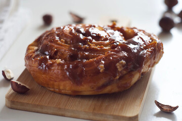 A bun with caramel and nuts lies on a board on the table.