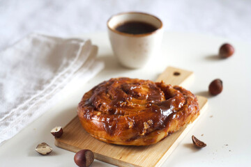A bun with caramel and nuts lies on a board on the table.