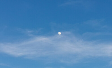 La Luna di giorno nel cielo azzurro dietro al velo di una nuvola