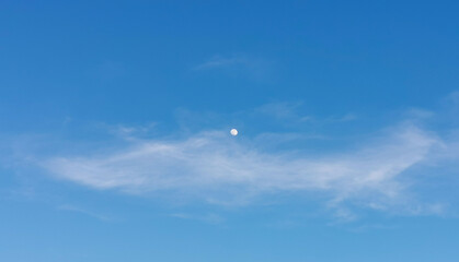 La Luna di giorno nel cielo azzurro dietro al velo di una nuvola
