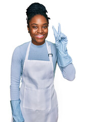 Young african american woman wearing apron smiling with happy face winking at the camera doing...