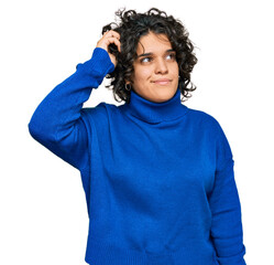 Young hispanic woman with curly hair wearing turtleneck sweater confuse and wondering about...