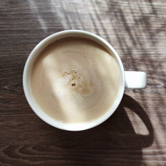 coffee cup with cappuccino in sunlight on wooden brown table, square photo