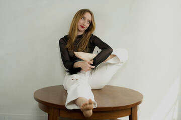 Young Blonde Woman in Black Lacy Top and White Jeans Poses in a Studio Setting
