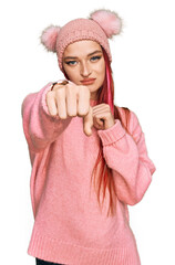 Young caucasian woman wearing casual clothes and wool cap punching fist to fight, aggressive and angry attack, threat and violence