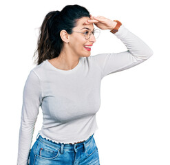 Young hispanic woman wearing casual clothes very happy and smiling looking far away with hand over...