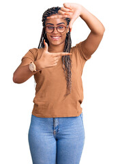 Young african american woman with braids wearing casual clothes and glasses smiling making frame with hands and fingers with happy face. creativity and photography concept.