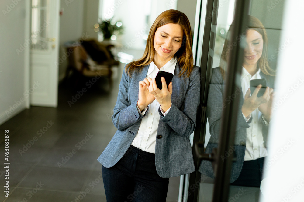 Wall mural Smiling Businesswoman in Modern Office Holding Smartphone Enjoying a Successful Work Day