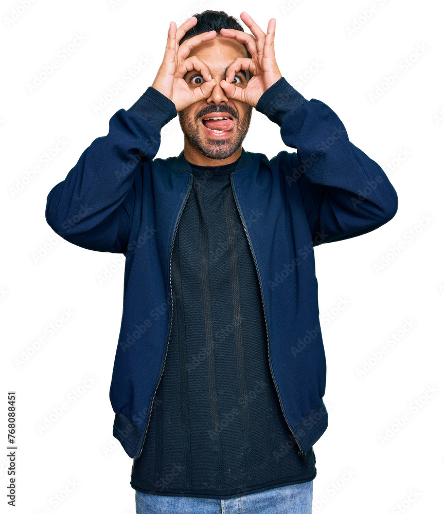 Poster Young hispanic man wearing casual clothes doing ok gesture like binoculars sticking tongue out, eyes looking through fingers. crazy expression.