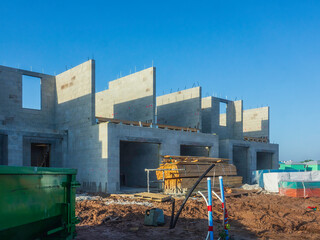 Fototapeta premium Construction site of multiple single-family housing units, with wrapped and unwrapped stacks of lumber, utility connections (middle foreground), and dumpster (bottom left), in southwest Florida