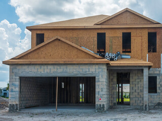 Single-family house under construction, with rolls of protective wrap for use on roof and particle-board exterior above concrete shell, in a suburban residential development in southwest Florida