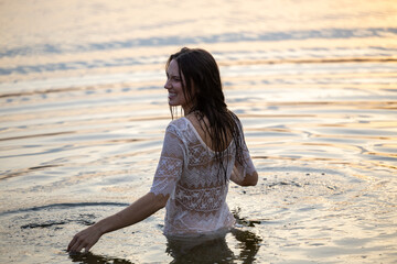 A girl in a white crocheted dress stands in the water in the evening light