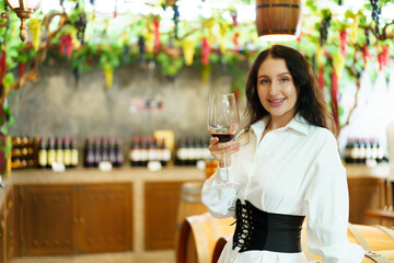 Portrait of beautiful caucasian young woman enjoy testing the red wine and showing a wine glass to camera. 