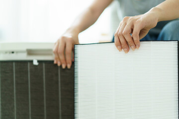Woman replaces a dirty and dusty air purifier filter in living room. 