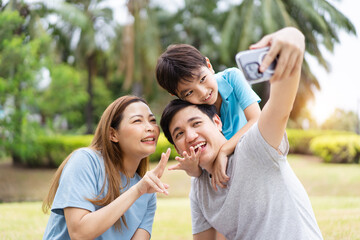 Fototapeta premium Happy cheerful Asian family with father, mother, and little son enjoy picnic together in a weekend at a park.
