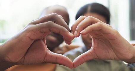 A diverse couple forms a heart shape with their hands - Powered by Adobe