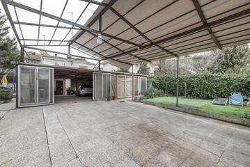 A covered terrace with a canvas roof on a metal structure and a room with aluminum doors and a vehicle parked inside