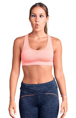 Young beautiful hispanic woman wearing sportswear making fish face with lips, crazy and comical gesture. funny expression.