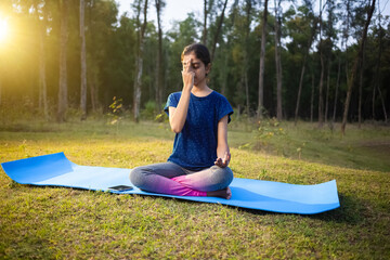 indian teenage girl self practicing pranayama breathing exercise in the forest at a morning sunrise...
