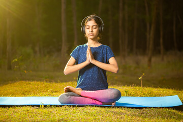 indian teenage athlete girl sitting in a zen-like position meditating while listening to relaxing...
