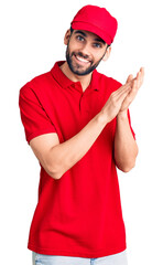 Young handsome man with beard wearing delivery uniform clapping and applauding happy and joyful, smiling proud hands together