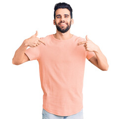 Young handsome man with beard wearing casual t-shirt looking confident with smile on face, pointing...