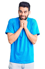 Young handsome man with beard wearing casual t-shirt laughing nervous and excited with hands on chin looking to the side