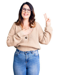 Beautiful young brunette woman wearing casual clothes and glasses smiling swearing with hand on...