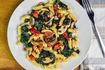 rotini pasta salad consisting of  spinach, tomatoes and mushrooms