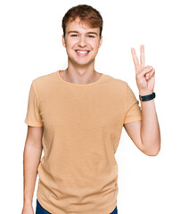 Young caucasian man wearing casual clothes showing and pointing up with fingers number two while smiling confident and happy.