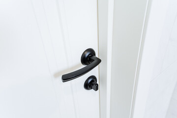Close up shot of a black door handle on a white wood door
