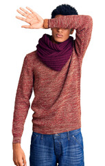 Young african american man wearing casual winter sweater and scarf covering eyes with arm, looking serious and sad. sightless, hiding and rejection concept