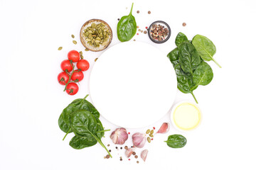 Round white plate with food ingridients tomatoes, spinach, oil, pumpkin seed, garlic, pepper on white background, top view,