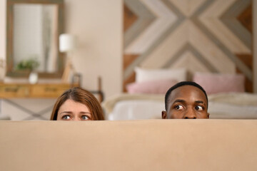 white woman and black man comically hiding behind the sofa