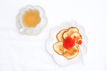  Pancakes with red caviar on white ceramic plate with green tea. White background. Copy space. Top view.