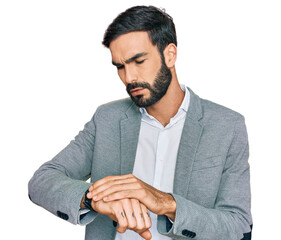 Young hispanic man wearing business clothes checking the time on wrist watch, relaxed and confident