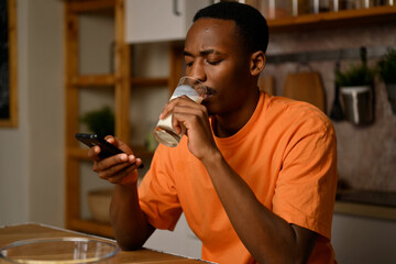 Young black guy drinks milk while sitting in the kitchen at the table. Slow motion