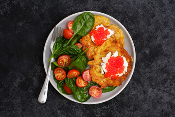 Fried potatoes pancakes with salmon caviar and cream cheese with spinach and tomatoes on black background.