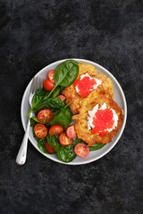 Fried potatoes pancakes with salmon caviar and cream cheese with spinach and tomatoes on black background.