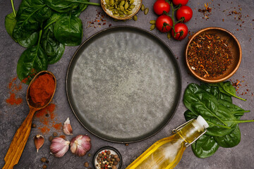 Round dark plate with food ingridients tomatoes, spinach, oil, pumpkin seed, garlic, pepper on dark background, top view,