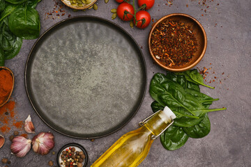 Round dark plate with food ingridients tomatoes, spinach, oil, pumpkin seed, garlic, pepper on dark background, top view,